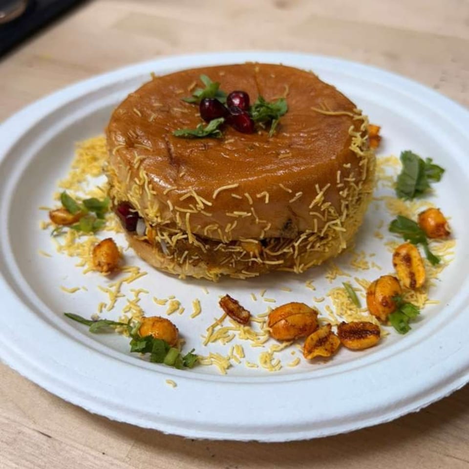A Dabeli burger, garnished with pomegranate seeds and cilantro, on a white plate.